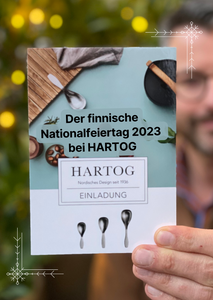 Wir laden Sie ein! Zu unserer Feier des finnischen Nationalfeiertags 2023 bei HARTOG. Hier hält Torben die Einladungs-Karte in das Bild. 